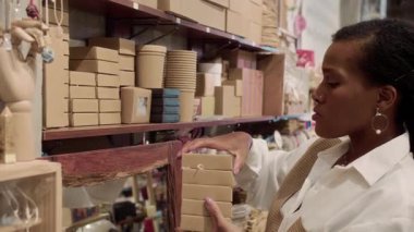 Orta boy Afro-Amerikalı bir kadının şık bluzuyla bijouterie mağazasındaki kutularla rafları düzenlerken.