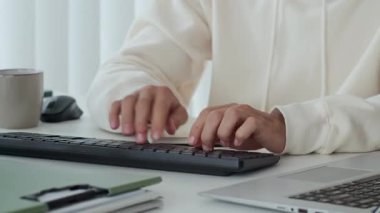 Bilgisayarın klavyesine yazı yazan ve ofis masasında yazı yazan isimsiz bir çalışanın el resimleri.