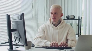 Ofisteki bilgisayarda rahat günlük kıyafet programındaki dövmeli beyaz adamın orta boy bıçak darbesi.