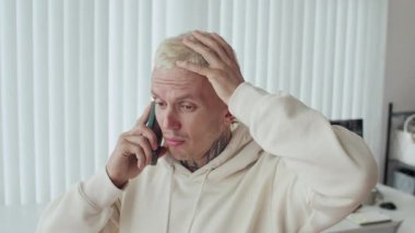 Ofisteki akıllı telefondan arayan endişeli erkek dövmeli beyaz müteahhit.