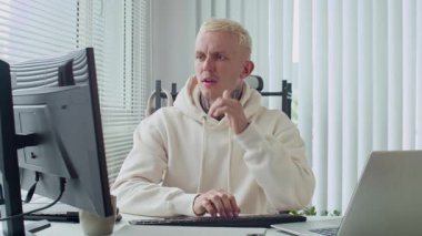 Beyaz kapüşonlu erkek, beyaz kapüşonlu programcı stresli görünüyor. Ofisteki bilgisayar ekranının önünde otururken kafasını tutuyor.