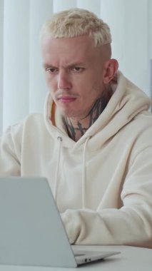 Ofisteki kablosuz dizüstü bilgisayarda dövmeli beyaz adamın dikey görüntüsü.