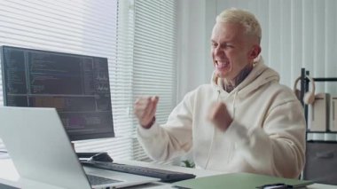 Ofiste masa başında kodlama senaryoları üzerinde çalışırken dövmeli bir uzmanın mutlu olduğu orta boy bir fotoğraf.