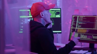 Kafkas dövmeli genç adam, neon ışıklı dijital cihazları hacklerken cep telefonuyla danışmanlık yapıyor.