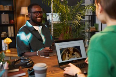 Genç adam, çevre ofisinde yeşil bitkilerle birlikte çalışırken meslektaşına gülümsüyor.