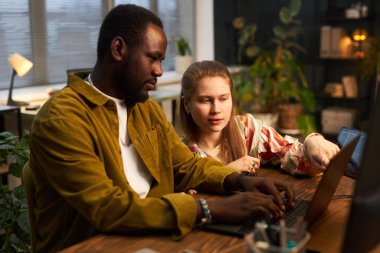 Ofisteki işleri sırasında dizüstü bilgisayarında kod yazarken programcıyla konuşan genç bir kadın.