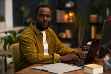 Afrika kökenli Amerikalı müdürün portresi ofiste oturuyor ve internette dizüstü bilgisayarla çalışıyor.