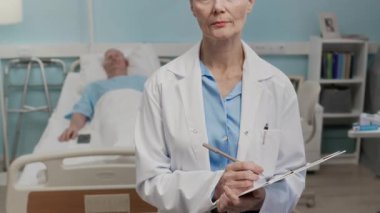 Yetişkin, beyaz kadın doktorun portresi hastane koğuşunda yatağında dinlenen yaşlı bir hastanın üniformasını dolduruyor.