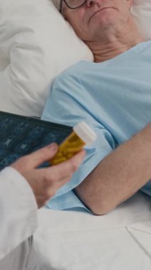 Doktorun MRI taramasıyla tablet tutarken dikey görüntüsü. Koğuştaki yaşlı hastaya reçete yazarken.