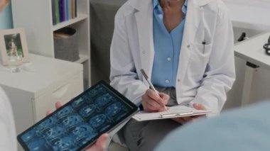 Klinikteki hastalarla tedavi planı hakkında konuşurken doktorların dijital tablet üzerinde MRI taraması kullanırken görüntüsü kesildi.