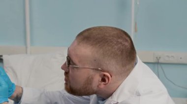 Hastane koğuşundaki yaşlı hastaların lenf düğümlerini elle muayene eden genç erkek doktorların orta boy yakın çekimi.