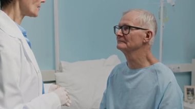 Beyaz önlüklü kadın doktor, yaşlı beyaz adamın boğazını muayene ederken elde çekilmiş bir fotoğrafı.