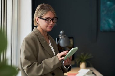 Ofiste çalışırken akıllı telefonunu kullanan gözlüklü bir iş kadını.