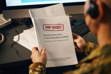 Askeri personel, gizli bir belgeyi ofis ortamında tutuyor ve inceliyor.
