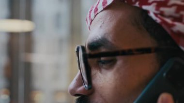 Geleneksel kıyafetlerle Orta Doğulu girişimcinin kapalı mekanda telefon konuşması yaptığı büyük bir yakın çekim.