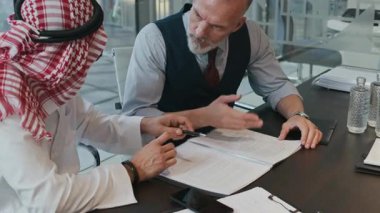 Modern ofiste masada otururken sözleşmenin şartlarını tartışan çeşitli erkek girişimcilerin yavaş hareketi