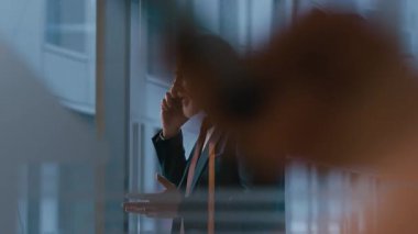 Orta yaşlı, beyaz takım elbiseli CEO 'nun modern ofis çalışma alanında telefon konuşması yaparken orta ölçekli bir fotoğrafı.