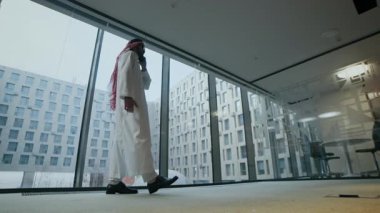 Geleneksel giysiler içinde, ofis koridorunda yürürken akıllı telefondan konuşan Orta Doğulu erkek girişimcinin zemin seviyesi.