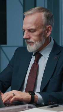 Ofisteki bilgisayarda çalışırken telefonla konuşan orta yaşlı beyaz girişimcinin dikey görüntüsü.