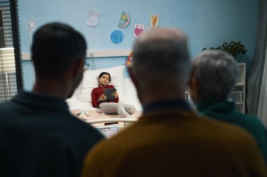 Akrabaların, hastaneye yatarken ve dijital tablet kullanırken küçük kızı izlemesi.
