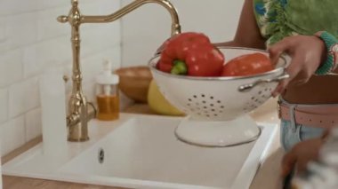 Ev mutfağında salata için taze sebze temizleyen tanınmayan bir aile fotoğrafı.