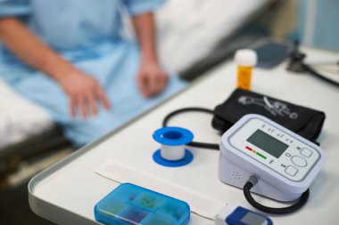 Tıbbi aletler ve ekipmanlar hastane odasındaki masada, arka planda hasta yatağında, sağlık hizmetleri aletleri düzgün bir şekilde sergileniyor.