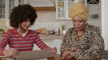 Çok ırklı anne ve kızının ev mutfağında birlikte masa peçetesi süslediği orta boy bir fotoğraf.