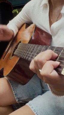 Gülümseyen Asyalı kadının arabada oturup akustik gitar çalarken araba yolculuğunun keyfini çıkardığı dikey çekim.