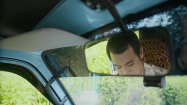 Yakışıklı ve gülümseyen Asyalı sürücü dikiz aynası ve minivan direksiyonunu ayarlıyor.