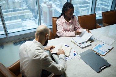 Meslektaşlarının not defterlerini incelemesi ve toplantı planlarını tartışması geniş açıdan görülüyor.