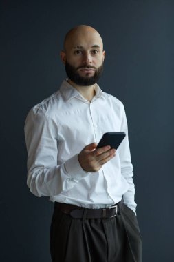 Genç işadamının portresi, arka planda dikilirken akıllı telefonunu kullanıyor.