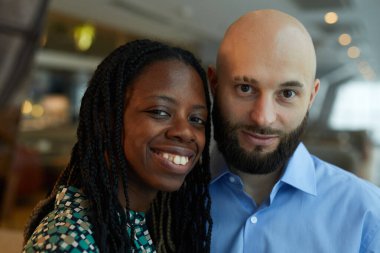 Restoranda vakit geçirirken kameraya gülümseyen çok ırklı genç bir çiftin portresi.