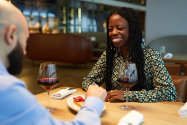 Lokantada bir erkekle yemek yiyen mutlu bir kadın. Masada oturup birbirleriyle konuşuyorlar.