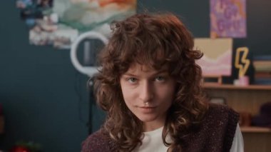 Kendine güvenen beyaz kıvırcık saçlı, septum piercingli, kameraya poz veren ve evi elleriyle kaplayan Z kızının yakın plan portresi.