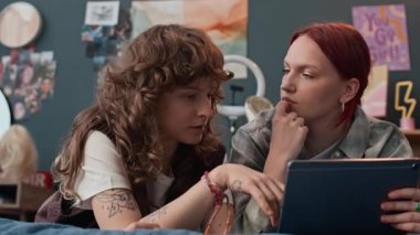 Dijital tableti tutan kızıl saçlı kız, makyaj ve maskeler tasarlama konusundaki düşüncelerini paylaşan bayan arkadaşını dikkatle dinliyor.