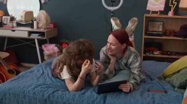 Dijital tabletle yatakta yatarken gülen ve sohbet eden iki neşeli zombi kadın arkadaş.