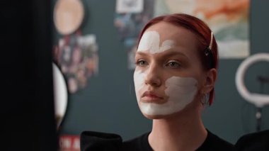 Kızıl saçlarını klipslerle örten ve makyaj malzemelerini yüz boyası çubuğuyla süren beyaz bir kızın aynasına ateş etti.