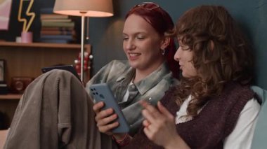 Evdeki yatakta dinlenirken dijital tablet ve akıllı telefondan internette sohbet eden ve sörf yapan iki beyaz kadın.