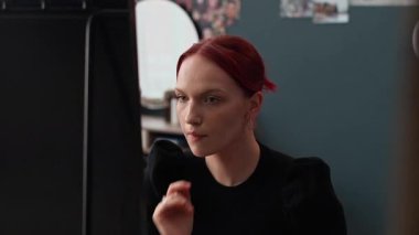 Kızıl saçlı, siyah kazak giyen, yüz derisini inceleyen ve saçlarını evdeki yansımasına bakarken ayarlayan Z gen kızının aynasına bak.