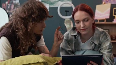 İki pozitif jenerasyon Z kız arkadaşı makyaj stilini tartışıyor. Yatakta yastıklarla yatarken dijital tablete bakıyorlar.