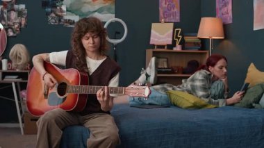 Kıvırcık saçlı, akustik gitar çalan genç bir kadın yatakta oturuyor, kız arkadaşı internette sörf yapıyor ve akıllı telefonuyla yaratıcı fikirleri paylaşıyor.