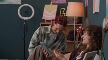 Neşeli bayan arkadaşlar birlikte evde vakit geçirirken gülüyor, konuşuyor ve akıllı telefon ekranlarına bakıyor.