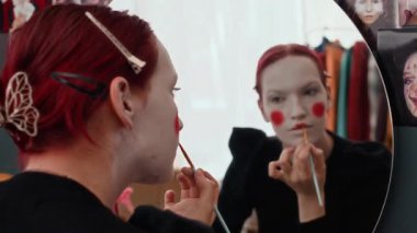 Kafkasyalı genç bir kadının görüntüsüne odaklan. Kırmızı dudak boyuyor. Aynaya bakıyor, evde palyaço makyajı yapıyor.
