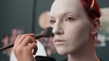 Makyaj fırçası kullanarak beyaz kostüm vakfını harmanlayan konsantre olmuş Kafkas 'lı genç kadının yakın plan fotoğrafı.