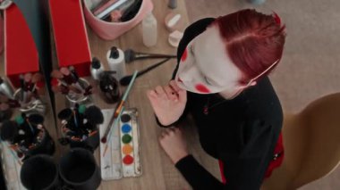 Kırmızı saçlı, palyaço makyajı yapan ve aynanın önünde kendini öpen genç bir kadının odasındaki makyaj masasında.