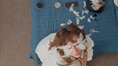 Temas lensleri ve yüzünde dekoratif tüylerle yatağında makyaj aletleriyle kameraya poz veren gizemli Z neslinin yüksek açılı portresi.