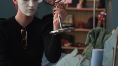 Kafkasyalı, kızıl saçlı, makyaj aynası alan ve beyaz kostümlü oyun vakfı uyguladıktan sonra sünger hareketini yapan genç bir kadın.