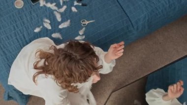 Beyaz kostümlü genç bir kadının, yatakta otururken yüzüne tüyleri yapıştırdıktan sonra aynada makyajını incelemesi.