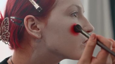 Beyaz yüz boyasının üzerine kırmızı daireler çizerken cadılar bayramı görüntüsü oluşturan beyaz Z jenerasyonlu kızın yakın plan görüntüsü.