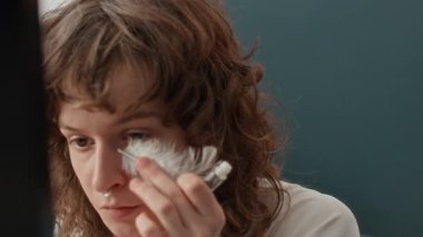 Kontak lensli ve burun delikli kıvırcık saçlı kızın aynasına yakından bak. Gözünün altındaki deriyle yüzleşmek için dekoratif tüy yapıştır.